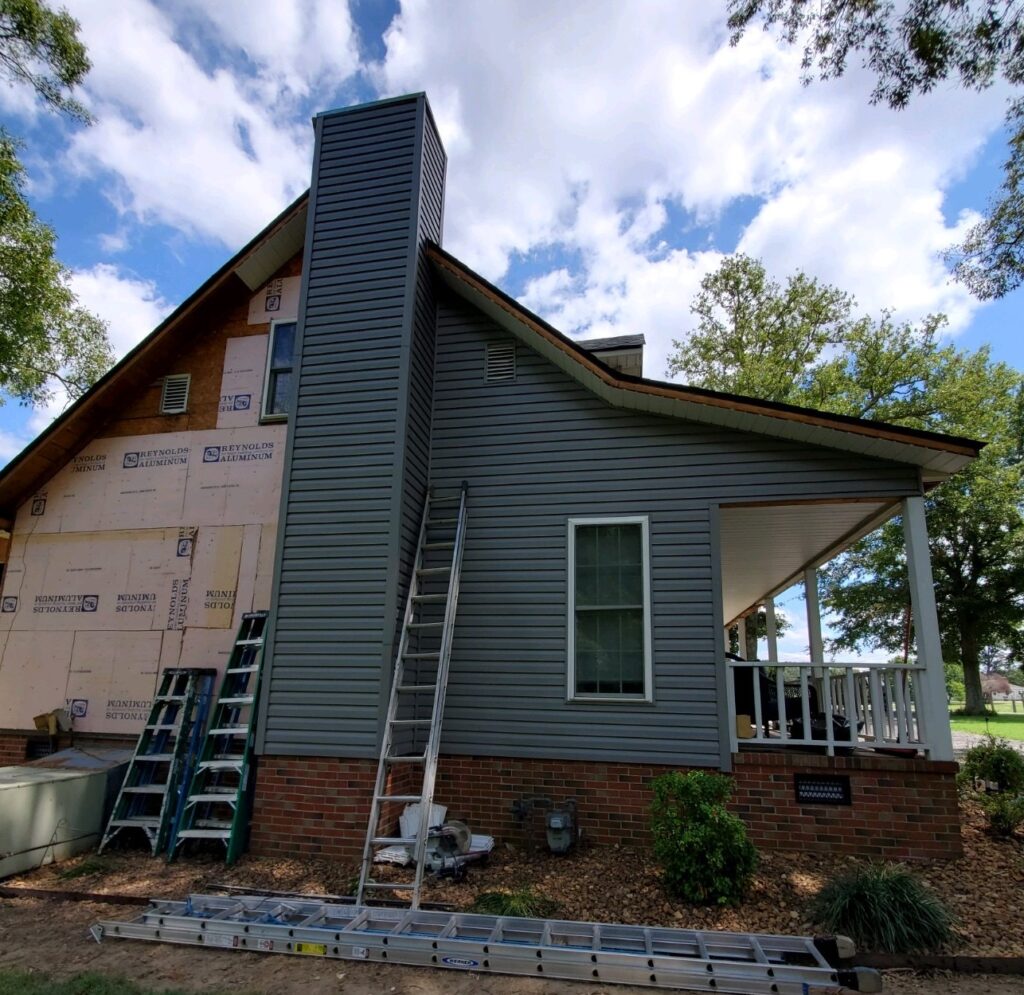 siding being installed on home with chimney and ladders visible