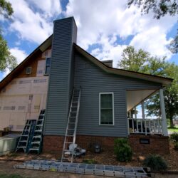 Siding being installed on home with chimney and ladders visible for Construction Services
