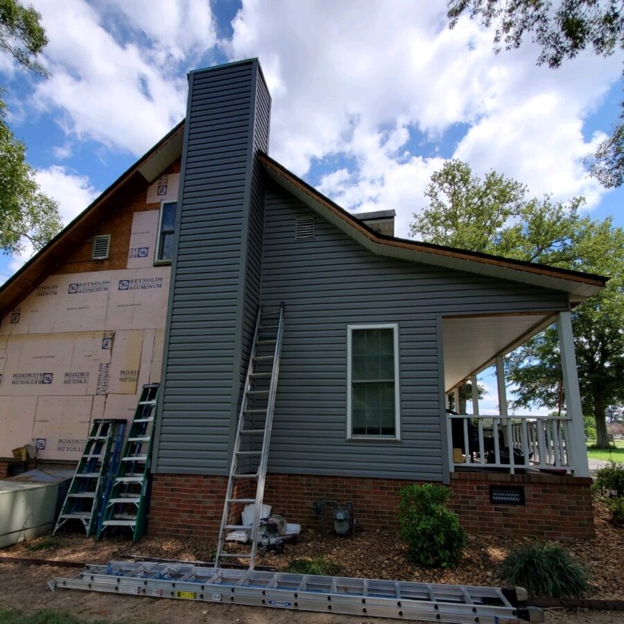 Siding being installed on home with chimney and ladders visible for Construction Services