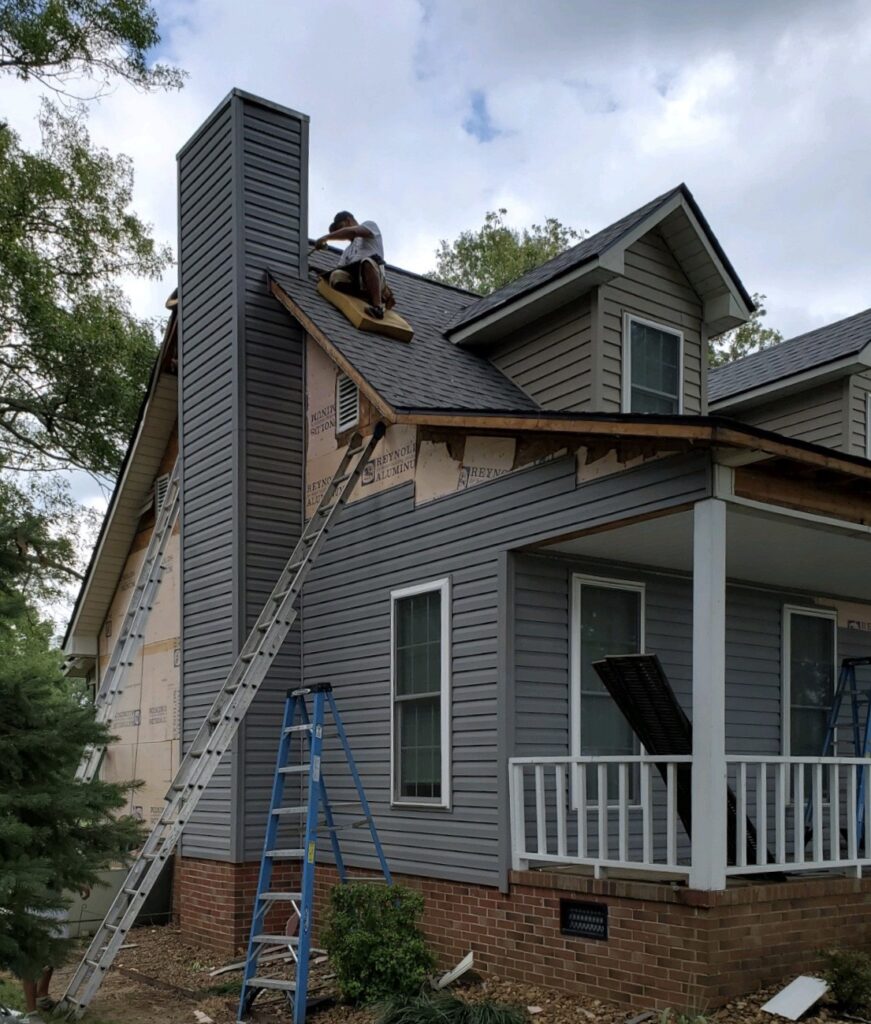 siding on home in progress with worker on roof and ladders visible